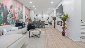 A modern living room with a large mural, a sofa, a coffee table, and a staircase leading to a dining area.