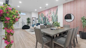 A modern dining area with a wooden table and chairs, a large painting on the wall, and a potted plant on the left.