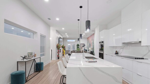A modern kitchen with white cabinetry, a central island, pendant lighting, and a view into the dining area.
