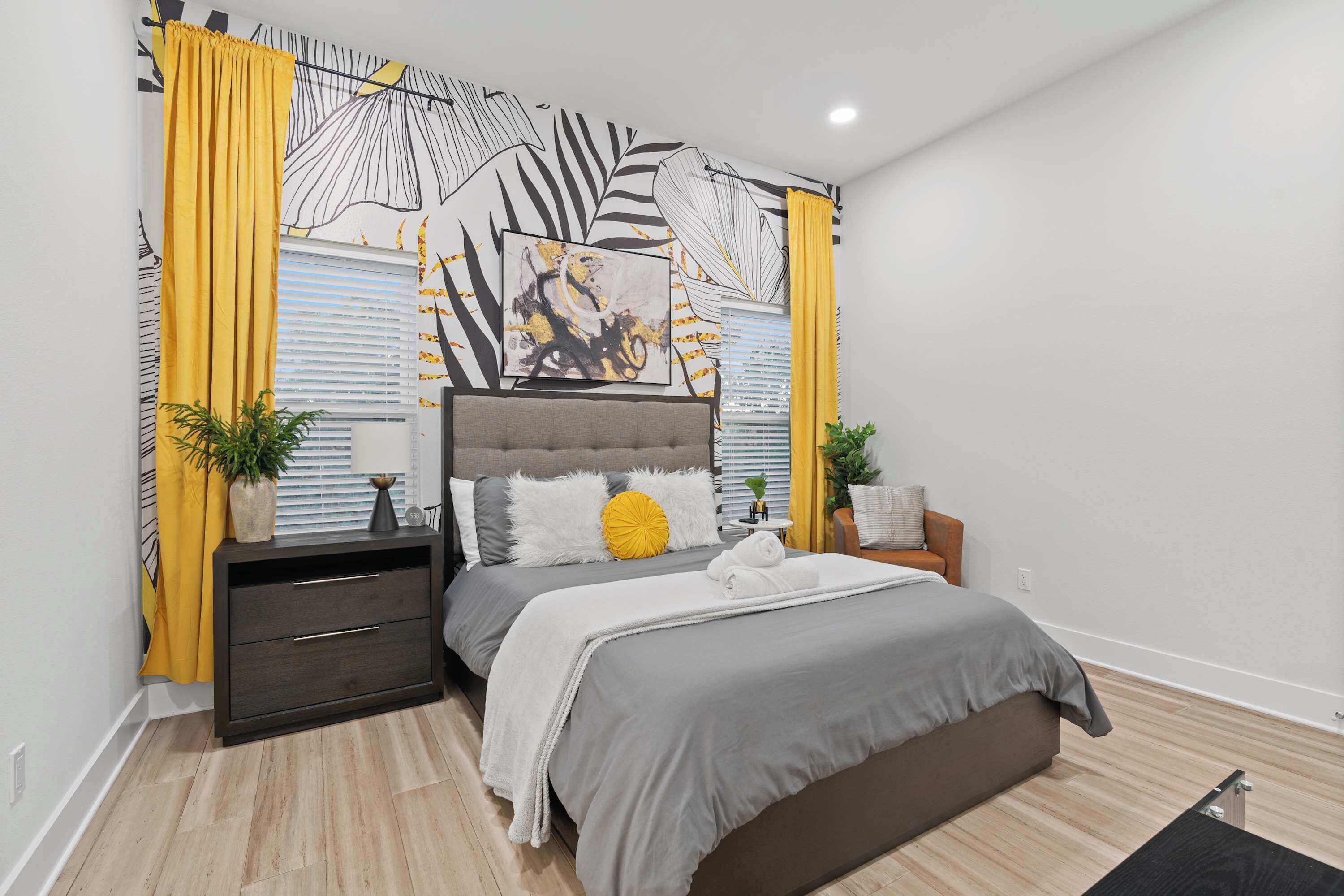 A modern bedroom with a grey bed, a grey headboard, and a large abstract painting on the wall.