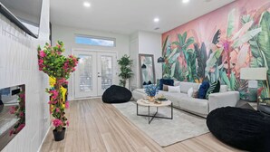 A modern living room with a white sofa, black bean bag chairs, a coffee table, and a large tropical mural.