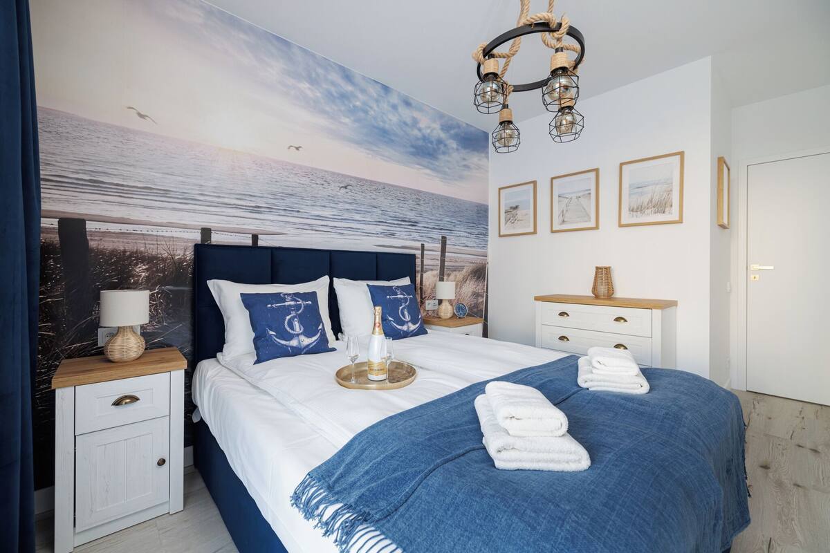 A bedroom with a large bed, a nightstand, a dresser, and a wall mural of a beach scene.