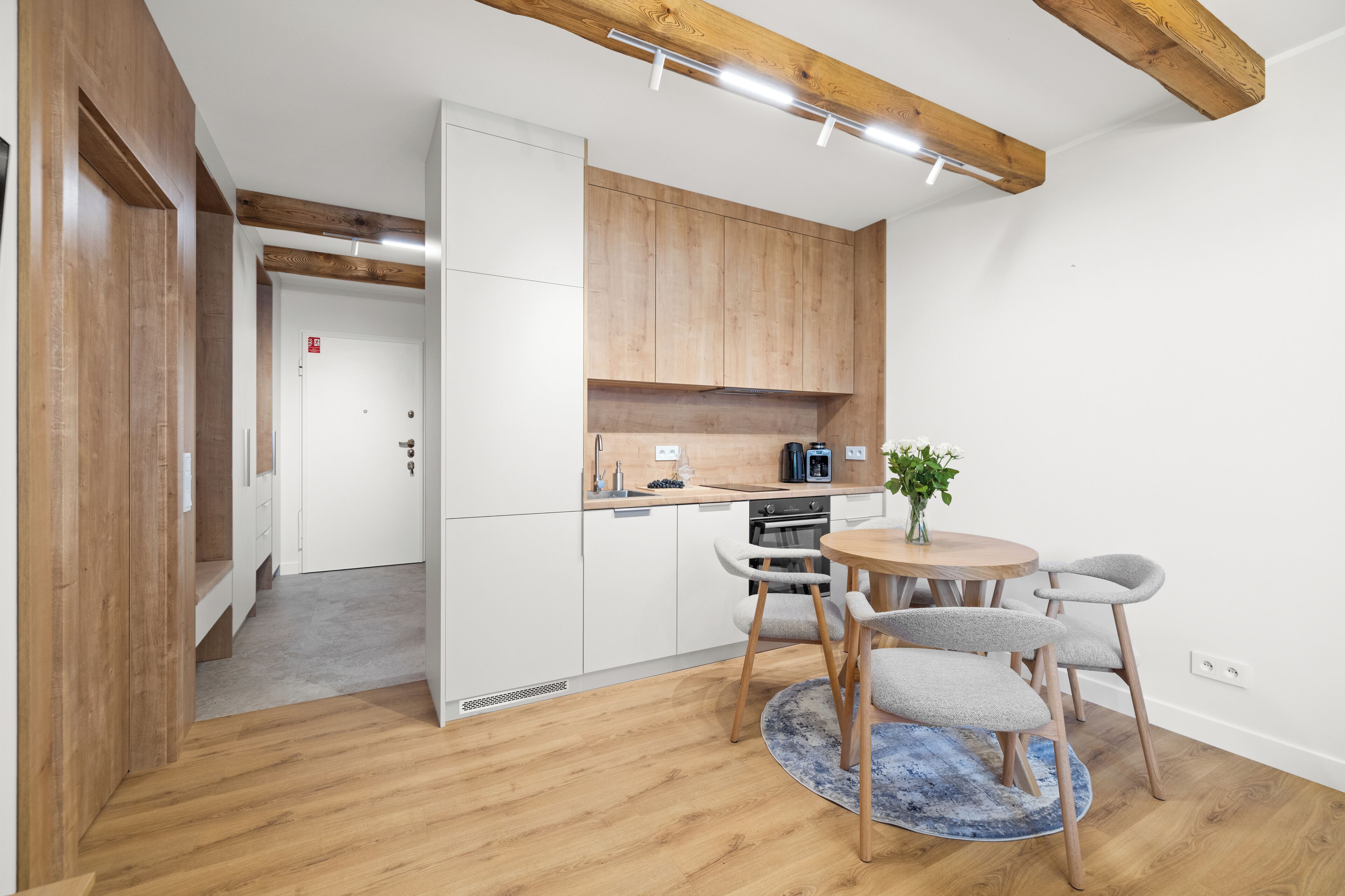 Eine moderne Küche mit Holzausstattung, ein Essbereich mit rundem Tisch und Stühlen sowie eine sichtbare Tür zu einem anderen Raum.