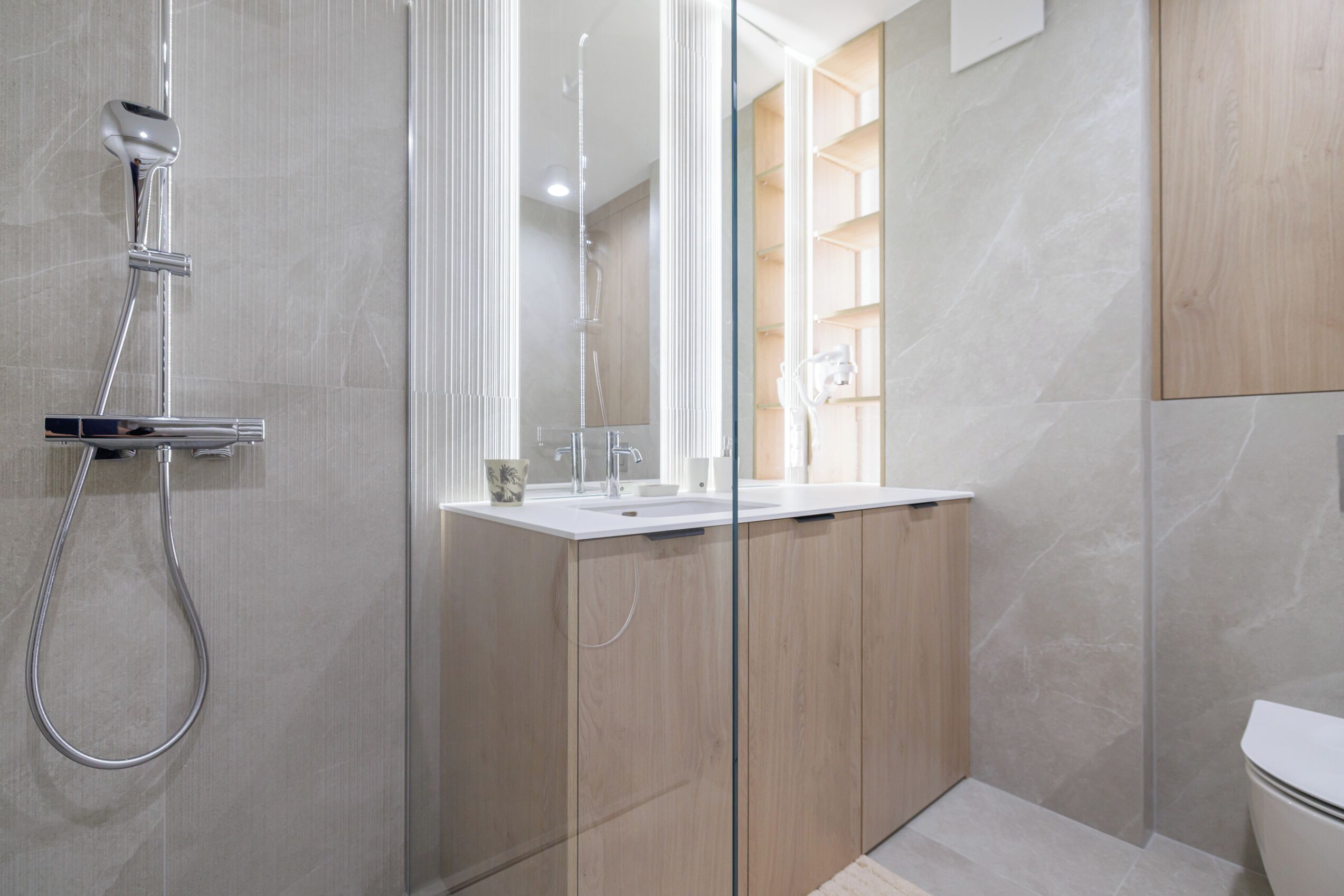 A modern bathroom with a glass shower enclosure, a white sink, and wooden cabinetry.