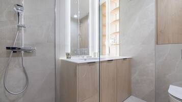 A modern bathroom with a glass shower enclosure, a white sink, and wooden cabinetry.