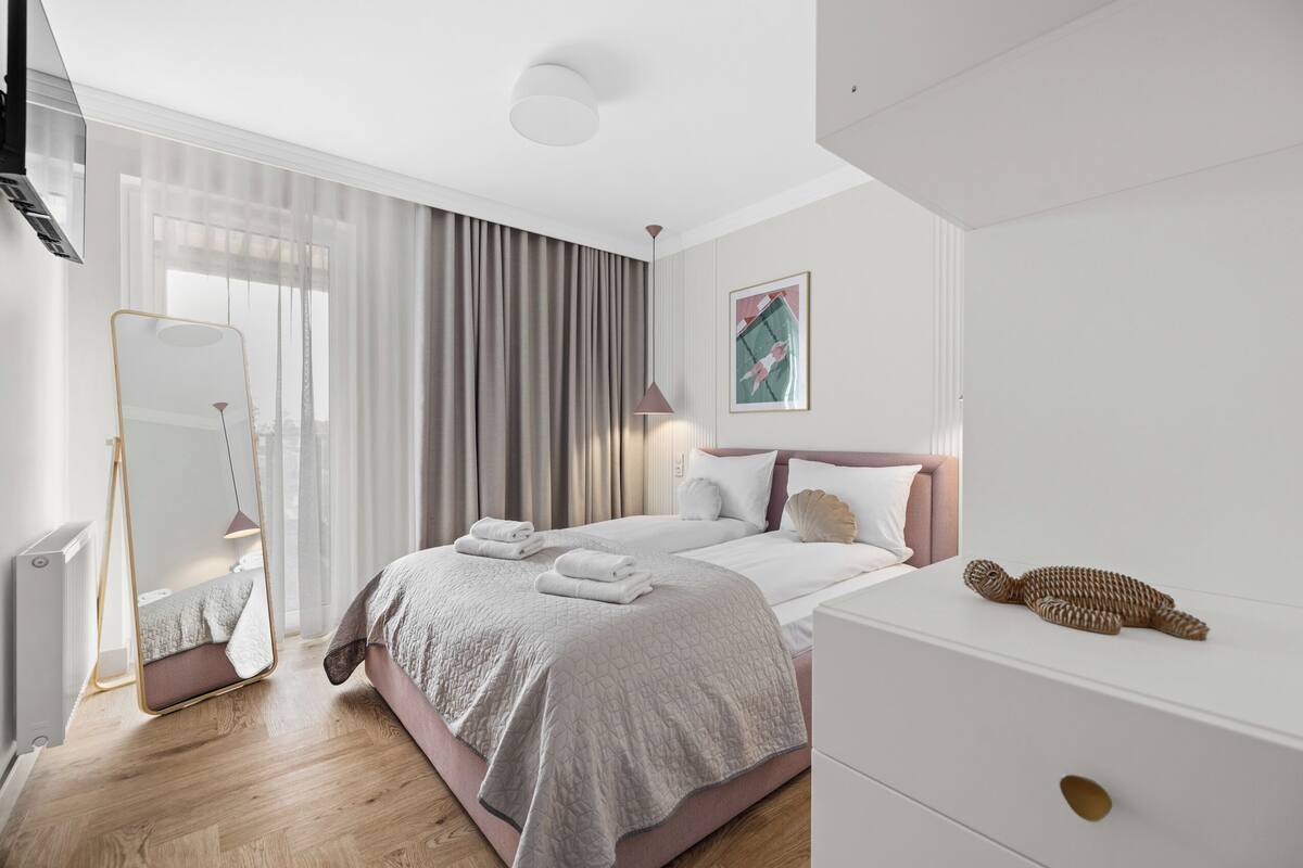 A modern bedroom with a large bed, bedside tables, a mirror, and a view of the outdoors.
