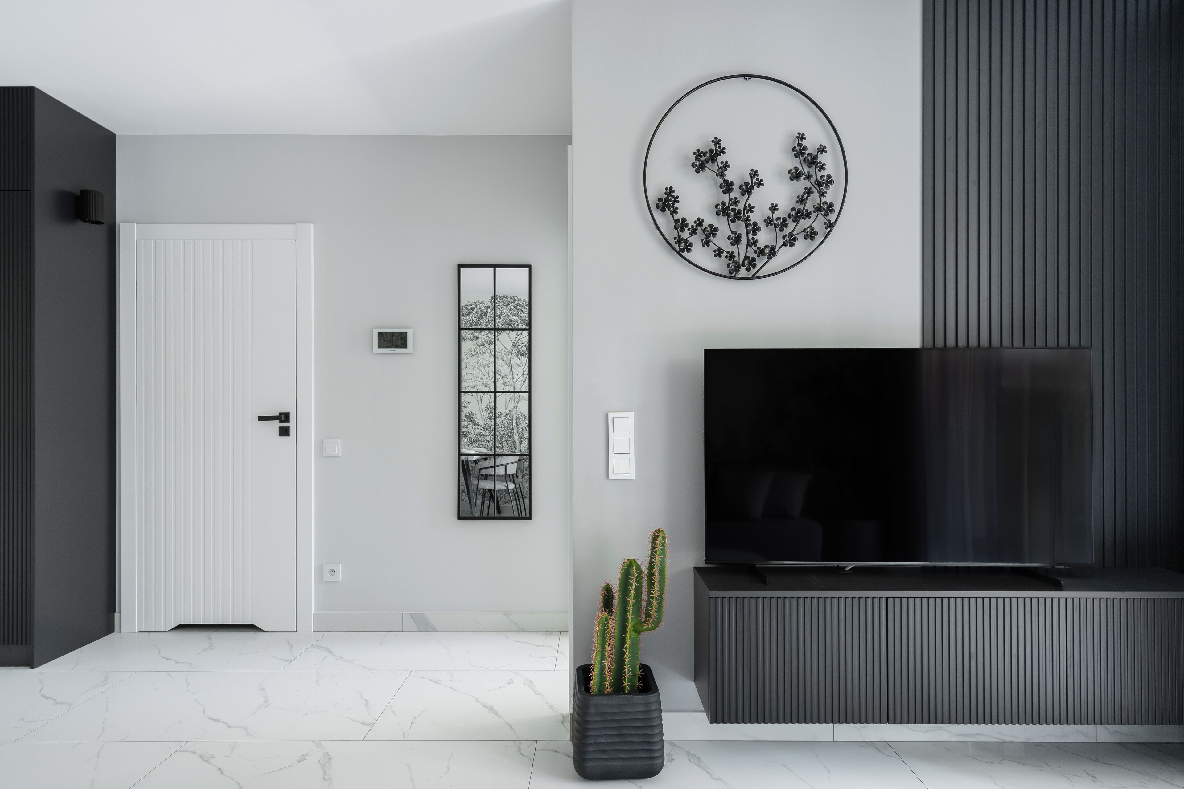 Un saló modern amb televisió de pantalla plana, una planta de cactus i una obra d'art circular penjada a la pared.