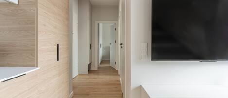 Un pasillo moderno con suelo de madera, paredes blancas y un televisor de pantalla plana montado.