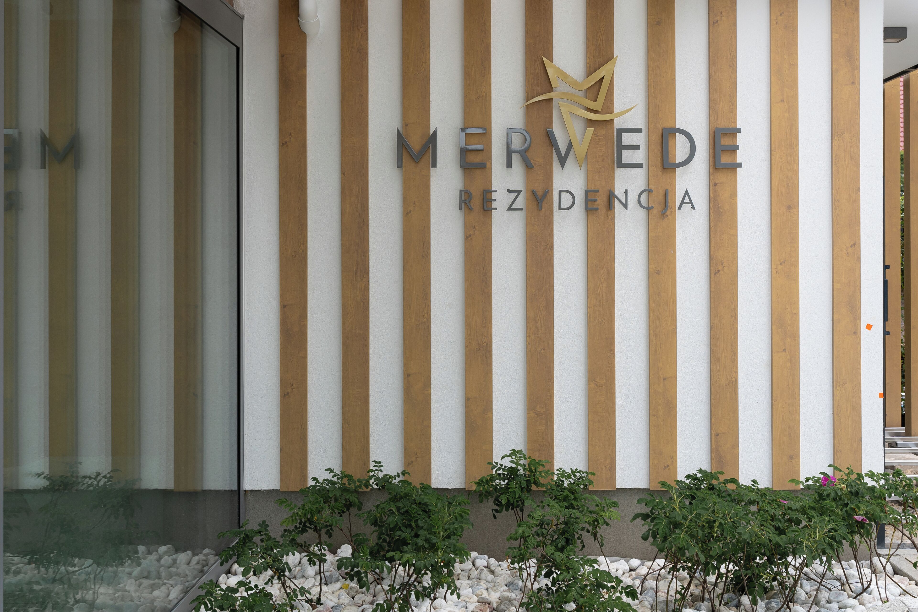 Een gevel met verticale houten panelen en de naam "MERWEDE REZYDENCIA" in grote letters.