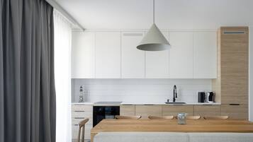 Moderni keittiö, jossa on valkoiset kaapit, puinen työtaso ja riippuvalaisin.