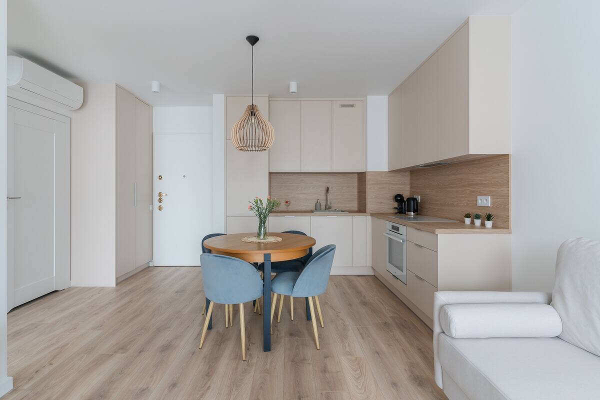 A modern kitchen with a round dining table, two blue chairs, and a white sofa.