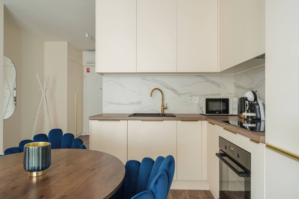 A modern kitchen with white cabinets, a marble backsplash, a gold faucet, a microwave, a coffee maker, and a dishwasher.