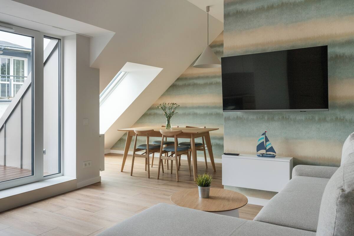 A modern living room with a large TV, a dining area with wooden furniture, and a view through a large window.