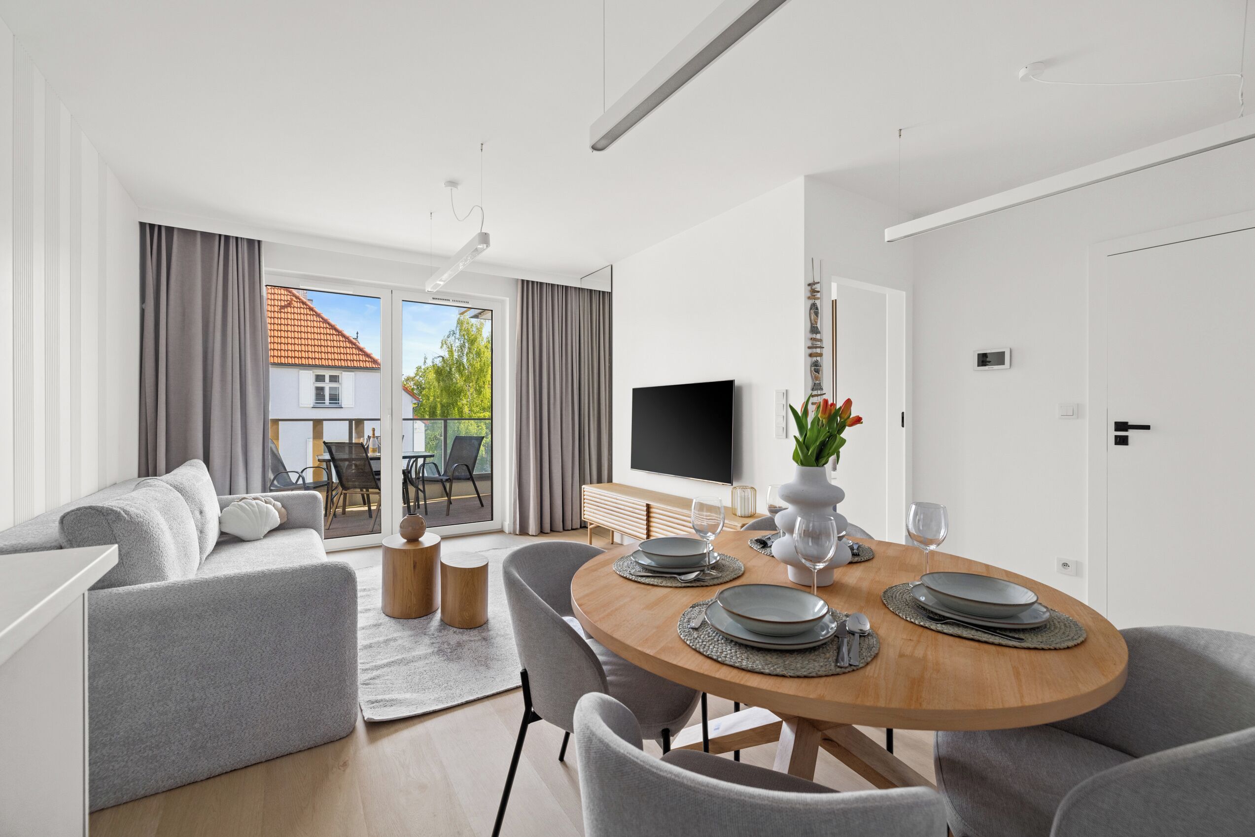 A modern living room with a dining area, a flat-screen TV, and a view of the outdoors.