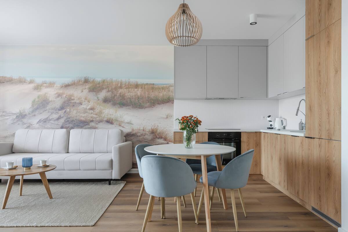 A modern kitchen with a view of the beach, a dining area with a round table and chairs, and a white sofa.