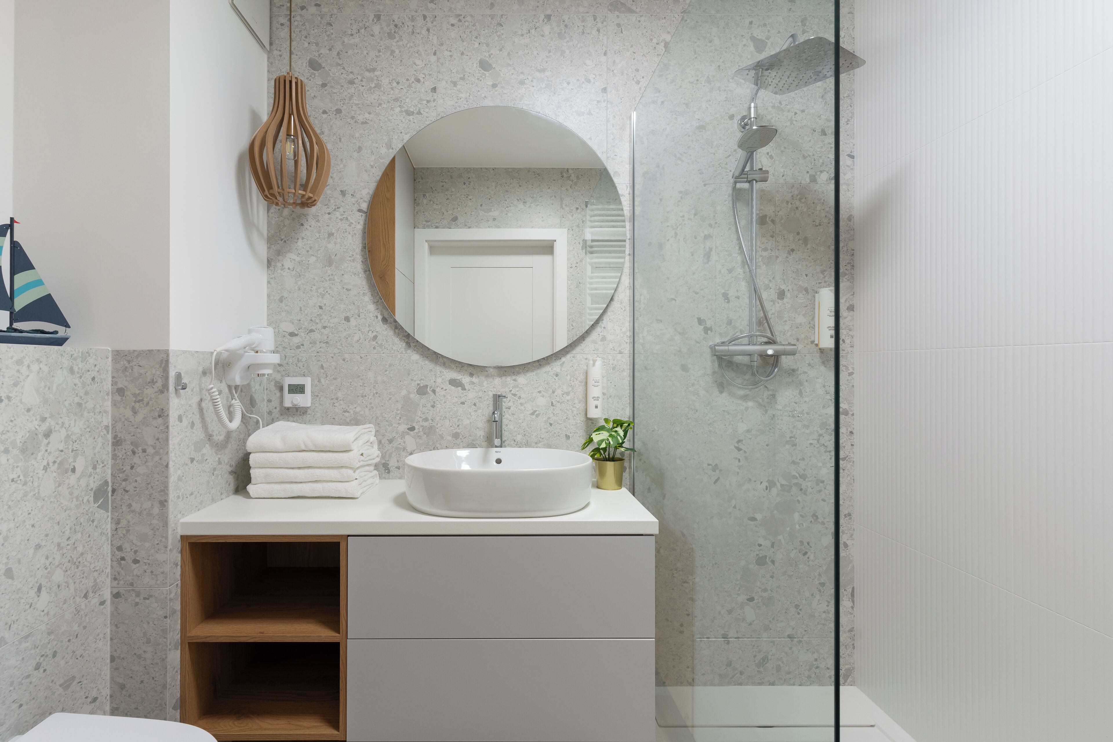 A modern bathroom with a round mirror, a white sink, and a shower.