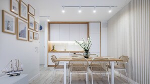 Een moderne eethoek met een houten tafel en rieten stoelen, een vaas met bloemen en ingelijste foto's aan de muur.