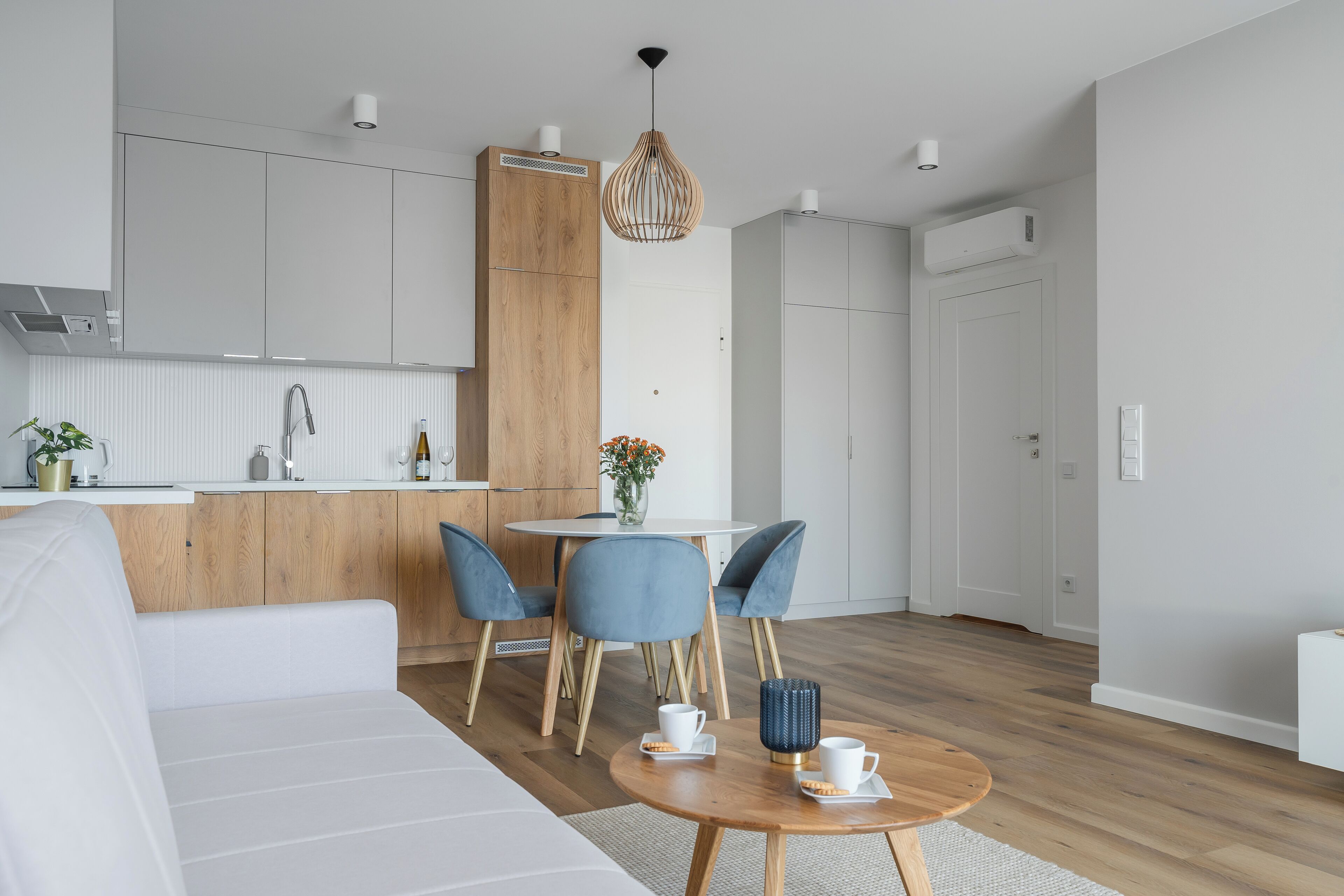 Una cocina moderna con armarios blancos, un muro decorativo de madera y una zona de comedor con sillas azules y una mesa redonda de madera.