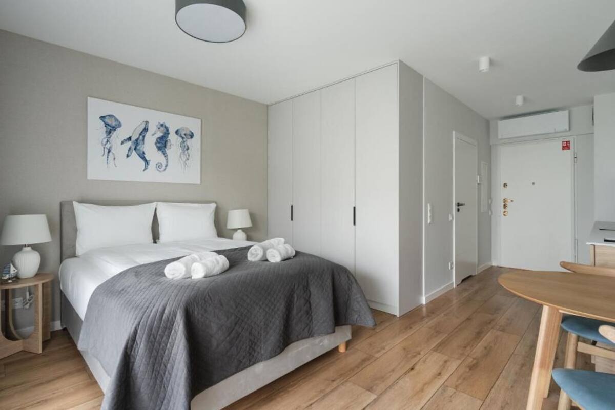 A modern hotel room with a large bed, a dining area, and a wardrobe.