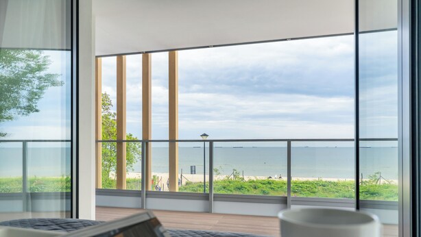 Een moderne kamer met grote ramen met uitzicht op een strand, een laptop en een kopje op de tafel.