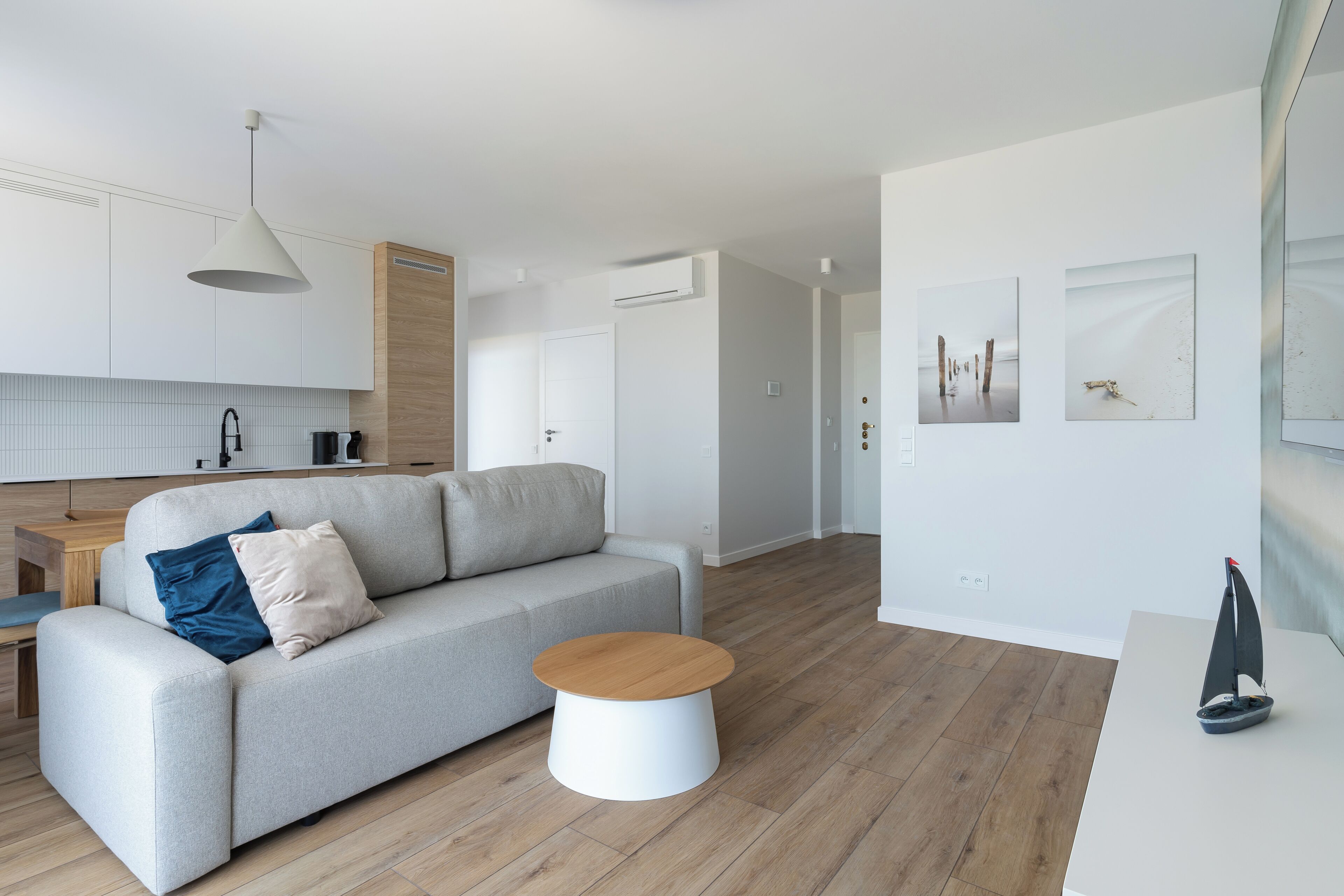 Ein modernes Wohnzimmer mit einem grauen Sofa, einem Holztisch und einem Modell eines Segelbootes auf einem weißen Tisch.