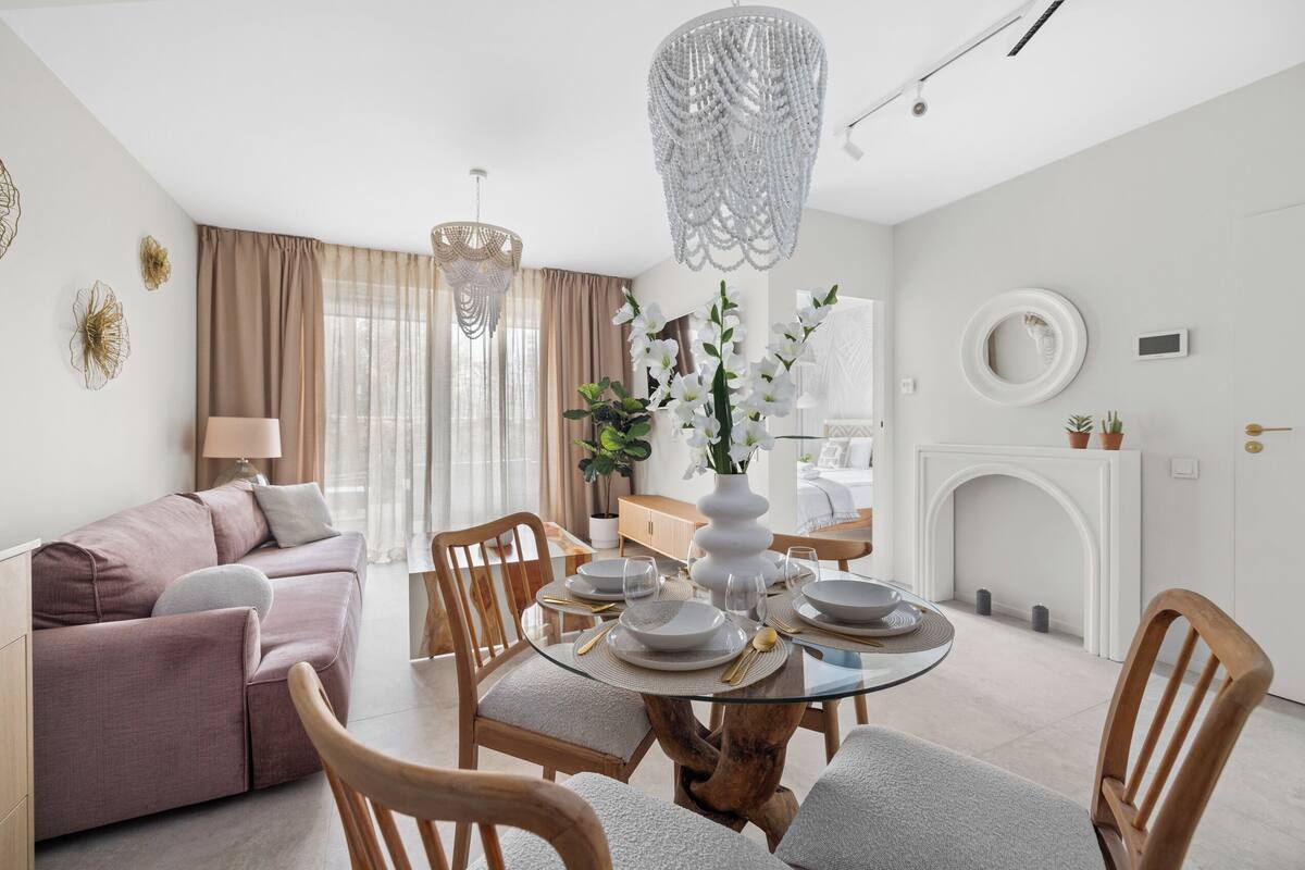 A modern living room with a round glass table, beige sofa, and a chandelier.