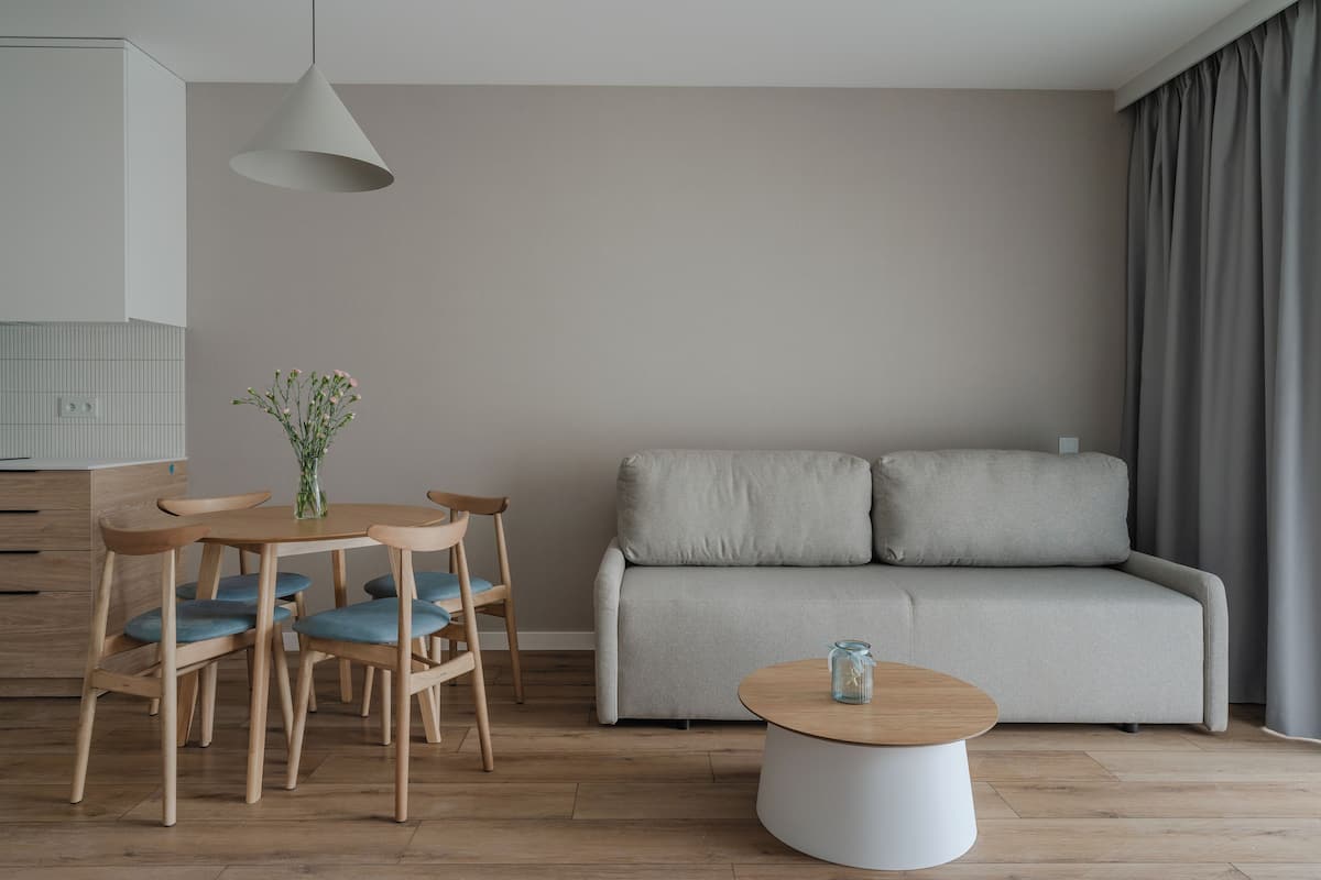 A modern living room with a grey sofa, wooden chairs, a round coffee table, and a hanging light fixture.