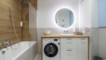 A modern bathroom with a built-in washing machine, a bathtub, and a sink.