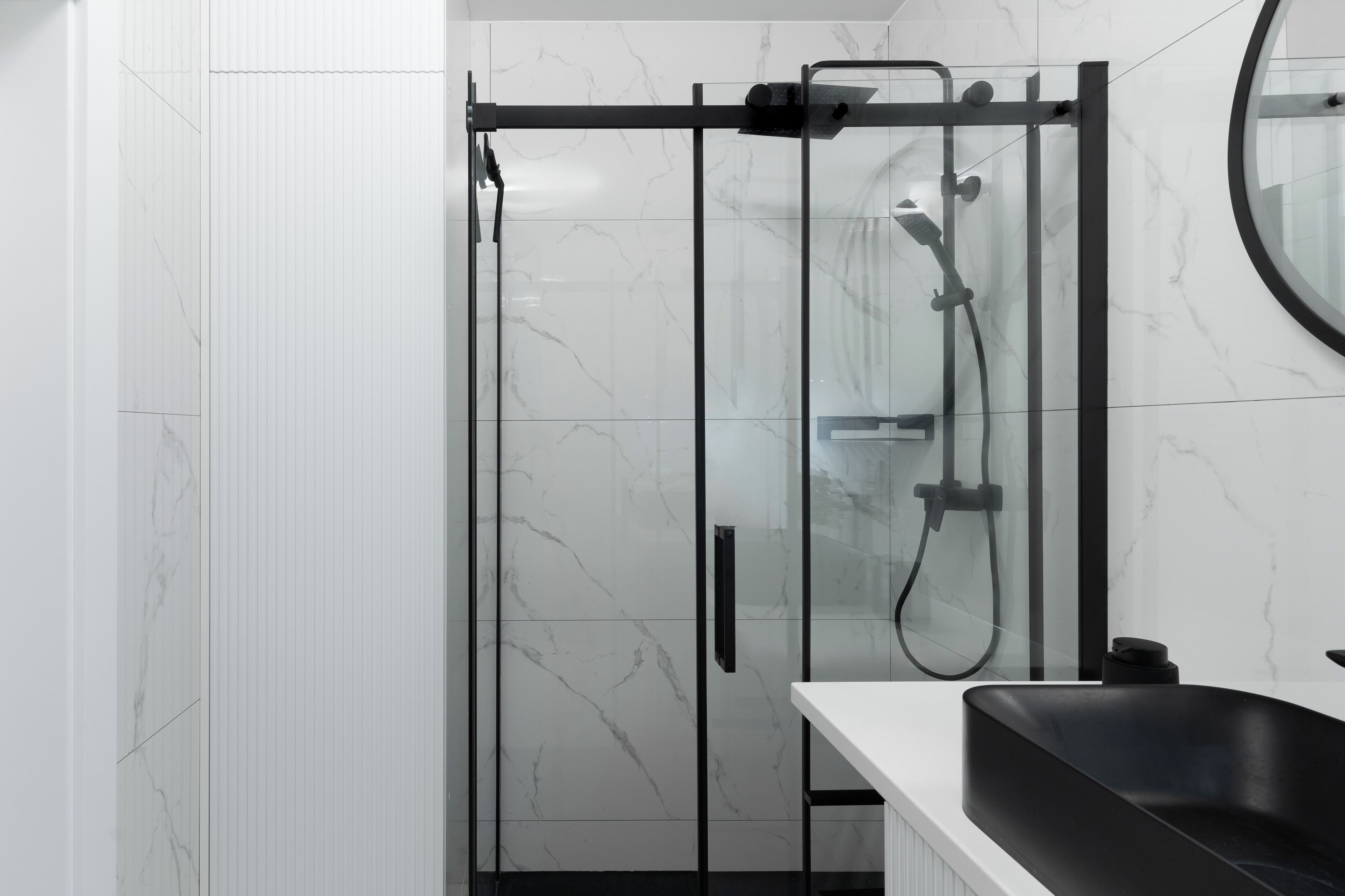 A modern bathroom with a glass-enclosed shower, a black sink, and a marble-tiled wall.