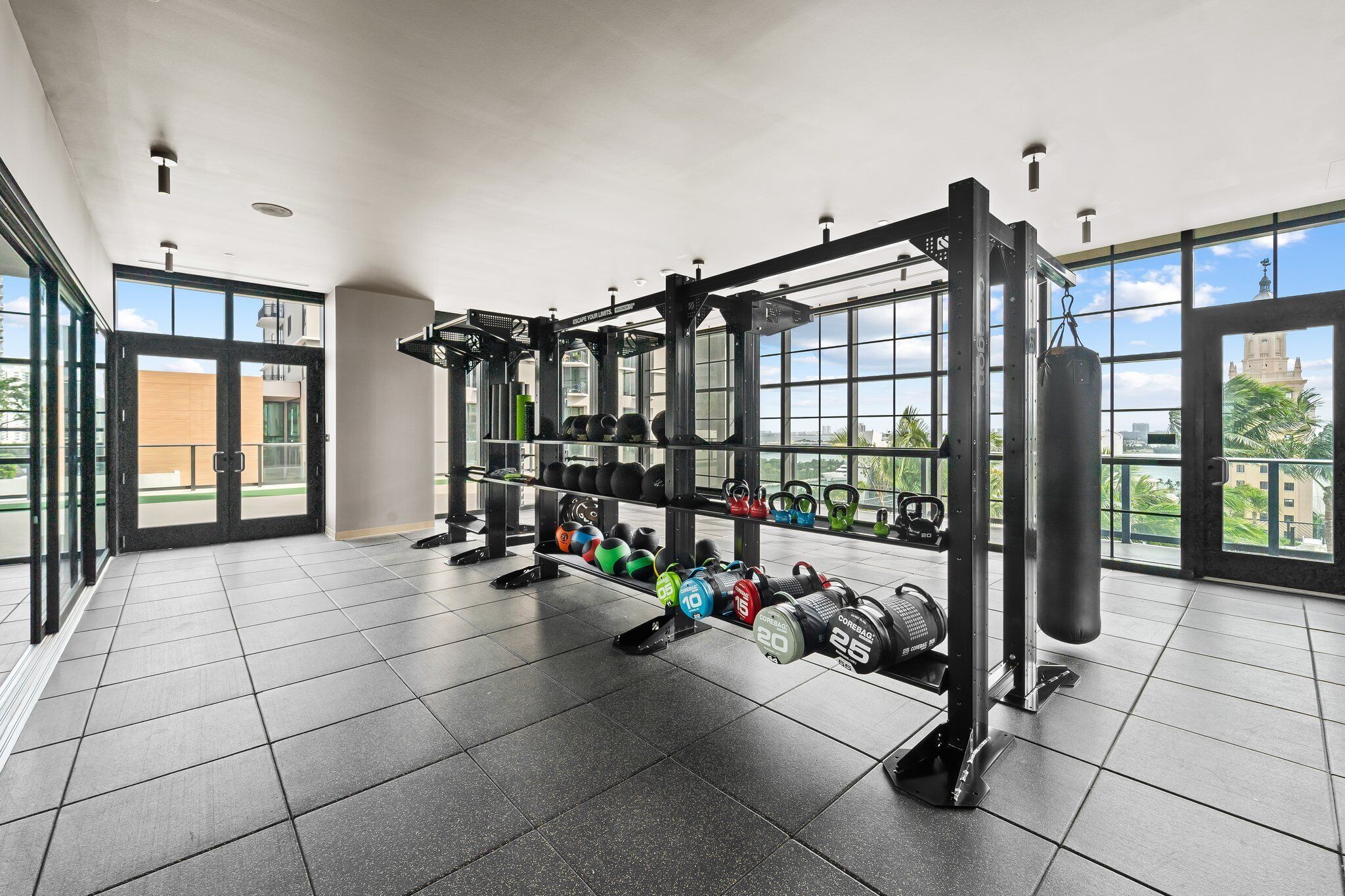 Une salle de sport équipée de matériel de musculation, dotée de grandes fenêtres et offrant une vue sur les bâtiments environnants.