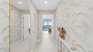 A hallway with a view to a dining area, patterned wallpaper, and a decorative console table.