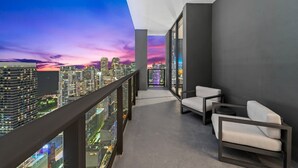 A balcony with a city view at dusk, featuring a modern design with a glass railing and minimalist furniture.
