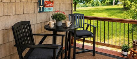 A wooden deck with two black chairs and a small table, a sign advertising live bait tackle, and a view of a green landscape.