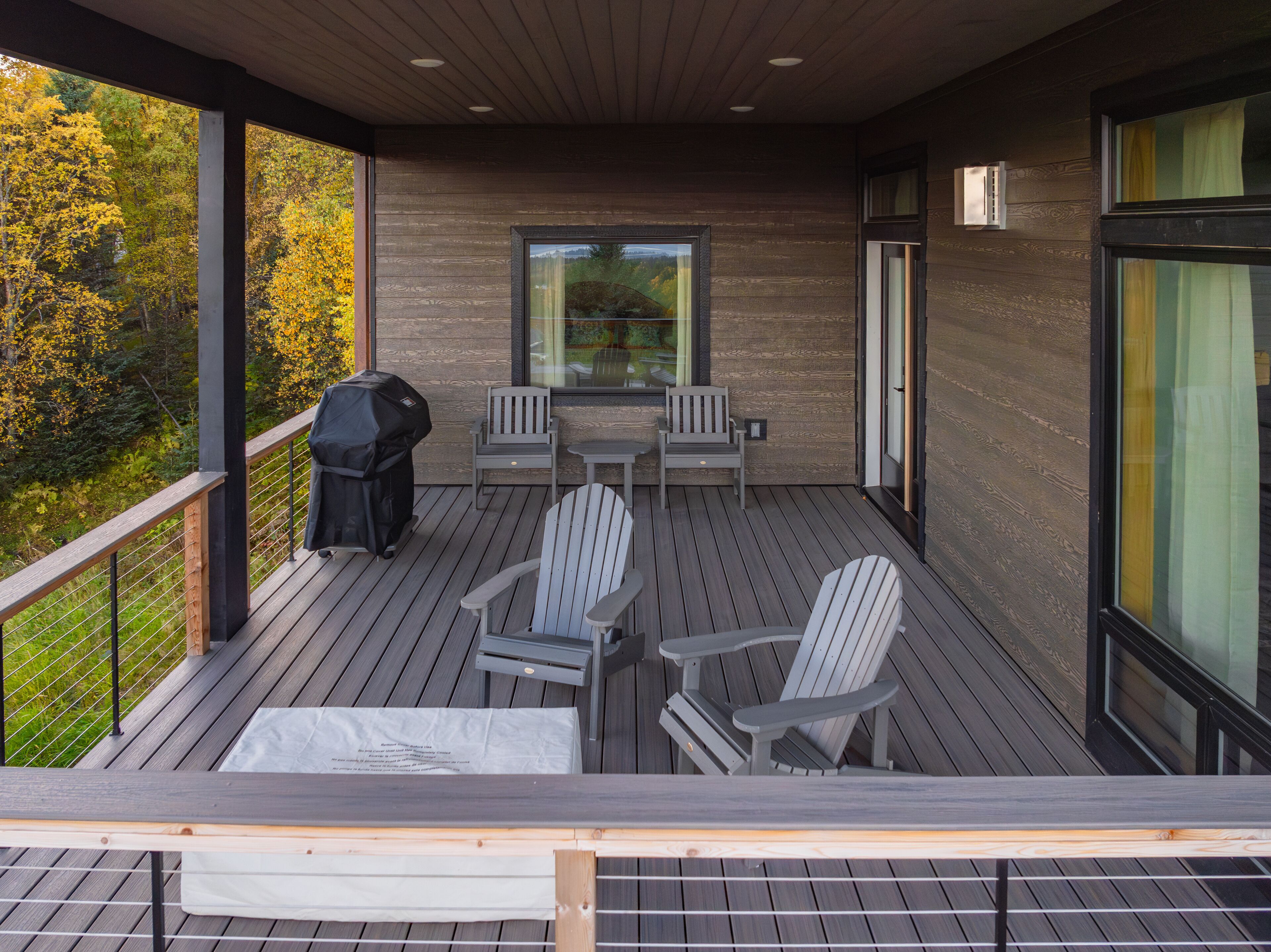 A covered deck with Adirondack chairs, a table, and a grill.