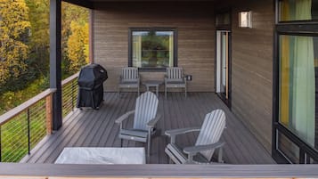 A covered deck with Adirondack chairs, a table, and a grill.