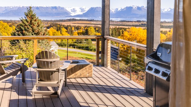 Une terrasse en bois avec un barbecue, des fauteuils Adirondack et une vue sur les montagnes et les couleurs automnales.