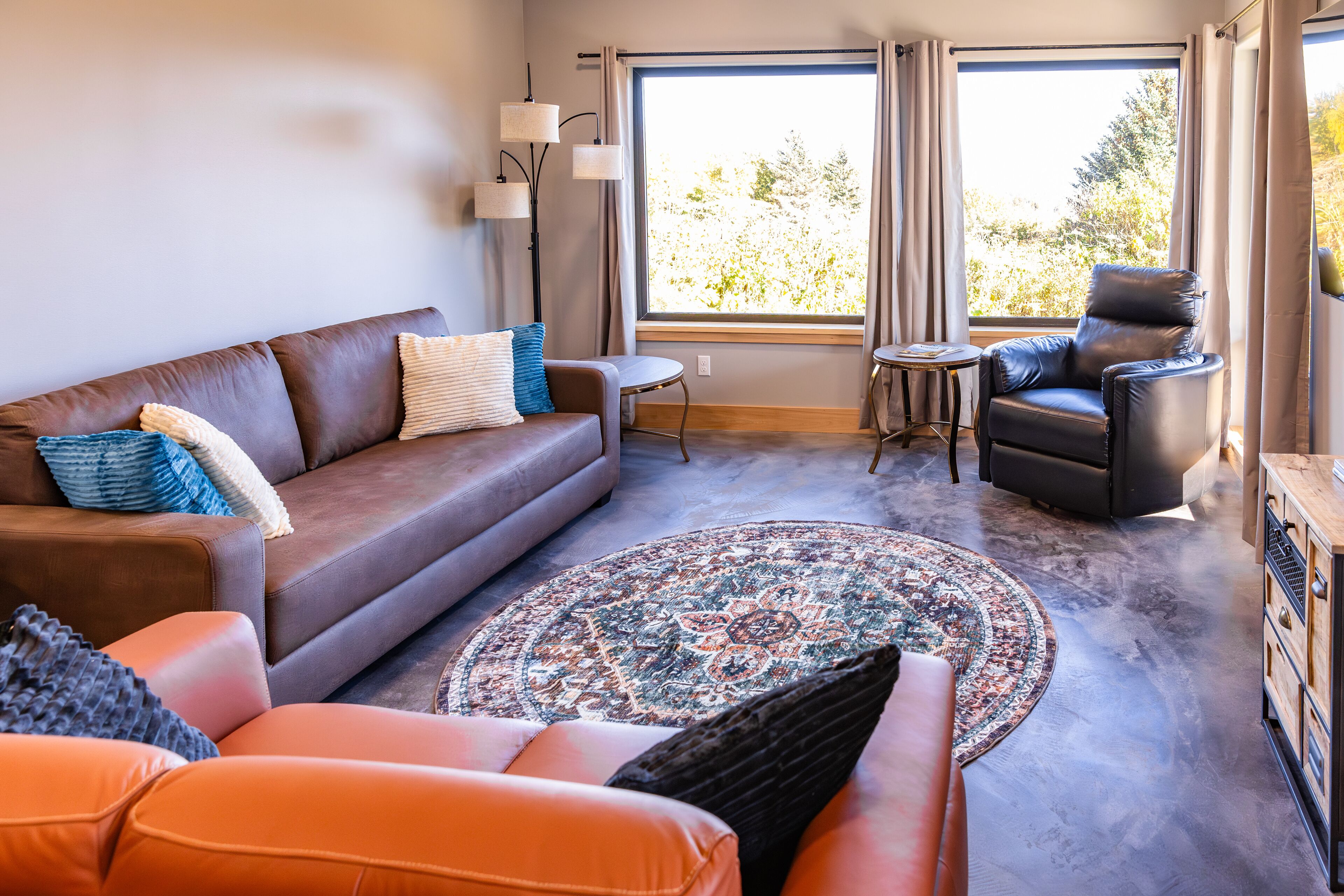 A living room with a brown leather sofa, a blue and white patterned rug, a black leather chair, and a small round table.