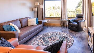 A living room with a brown leather sofa, a blue and white patterned rug, a black leather chair, and a small round table.