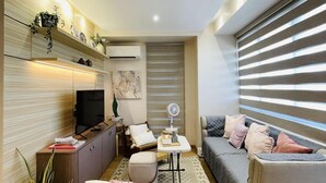 Un espacio habitable compacto con sofá, una mesita, televisor y una planta decorativa.