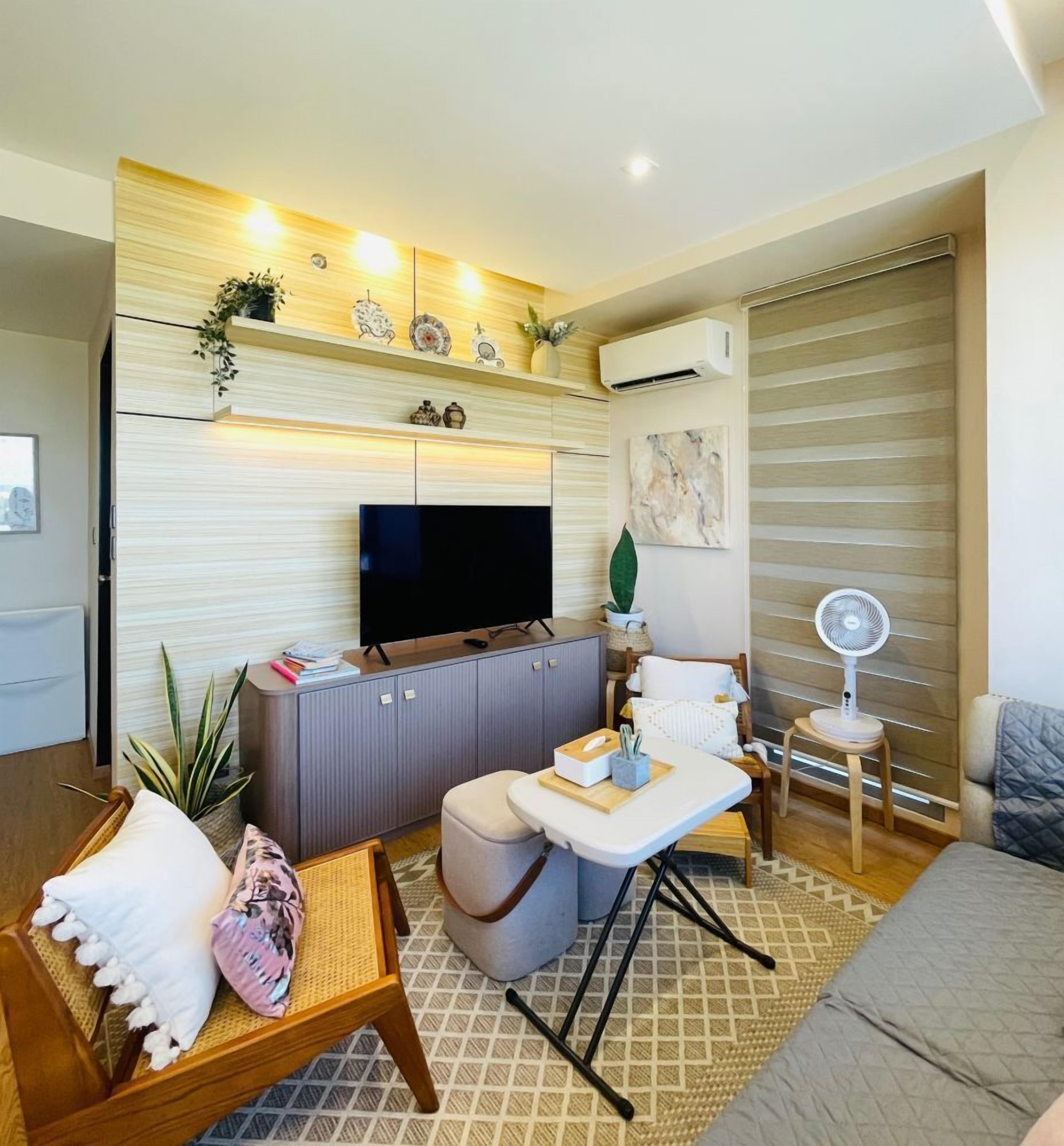 Una sala de estar moderna con un televisor de pantalla plana, un sofá, una mesa de centro y un pequeño ventilador.