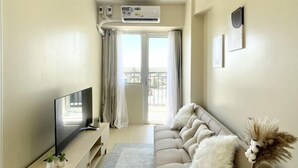 En moderne stue med et fladskærms-tv, en beige sofa, et træbord og en lille dekorativ skulptur.