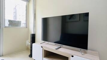 A modern living room with a flat-screen TV on a wooden TV stand, a small heater, and a window with blinds.