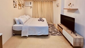 A bedroom with a bed, a TV, a shelf, and a window with curtains. - Modern Studio at Avida Towers Atria (Iloilo City)