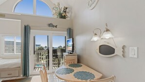 A room with a bed, a dining table with chairs, a TV, and a balcony with a view. - Plantation West 1367 (Gulf Shores)