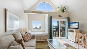 A modern living room with a sofa, a glass coffee table, a TV, and a balcony with a view. - Plantation West 1367 (Gulf Shores)