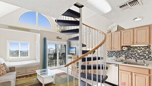 A modern apartment with a spiral staircase, a balcony with a city view, and a kitchen with wooden cabinets. - Plantation West 1367 (Gulf Shores)