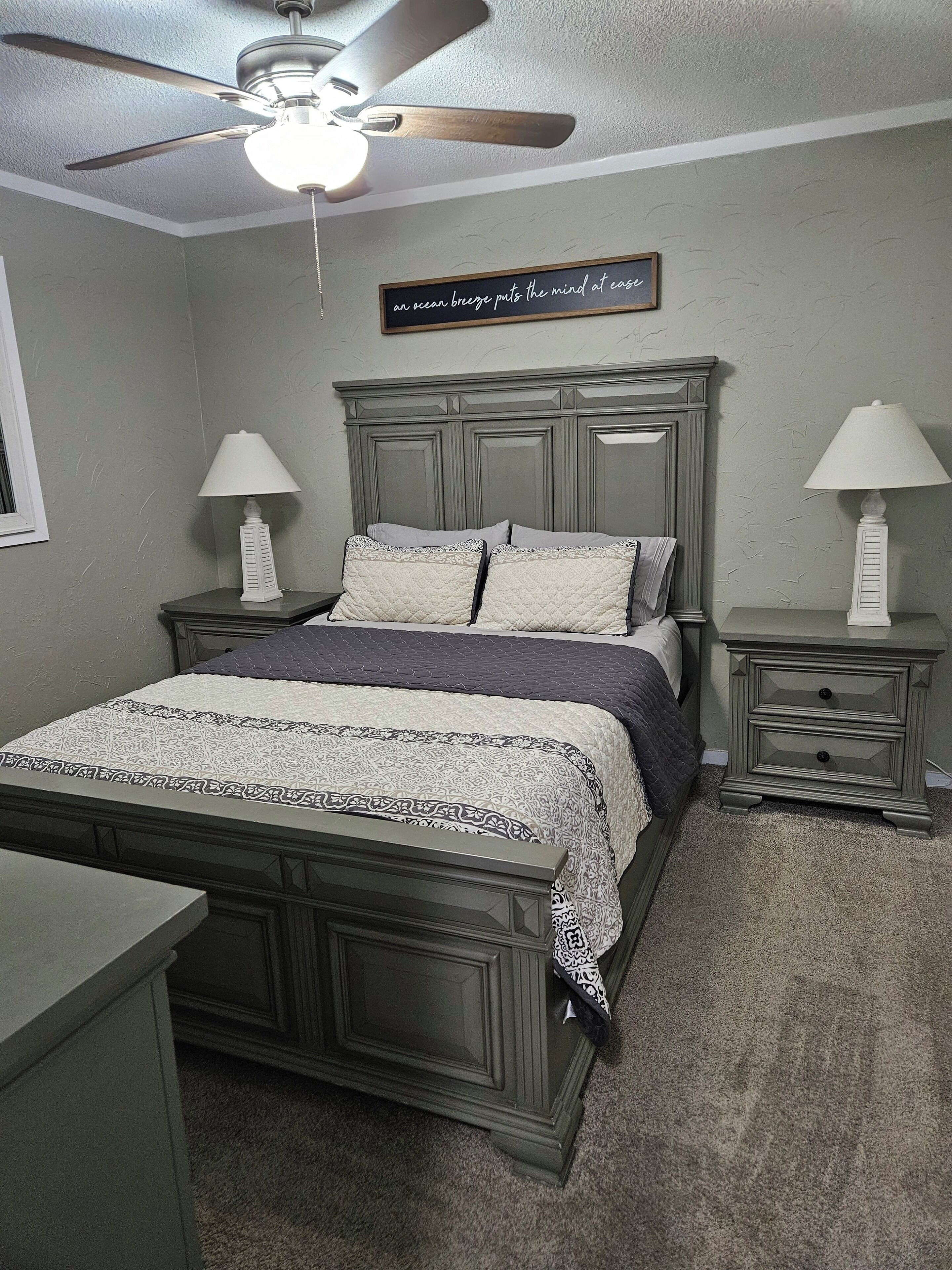 Ein Schlafzimmer mit einem Bett, zwei Nachttischen, einem Deckenventilator und einem an der Wand befestigten Schild.