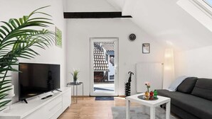 Ein modernes Wohnzimmer mit Flachbildfernseher, einer Couch, einem Couchtisch und einer Pflanze.