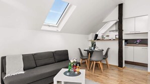 Ein modernes Wohnzimmer mit einem grauen Sofa, einem kleinen weißen Couchtisch und einem Essbereich mit Tisch und Stühlen. Über dem Essbereich ist ein Oberlicht zu sehen.