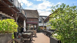 Ein Terrassenbereich im Freien mit Holztischen und -stühlen, umgeben von Gebäuden im rustikalen Baustil.